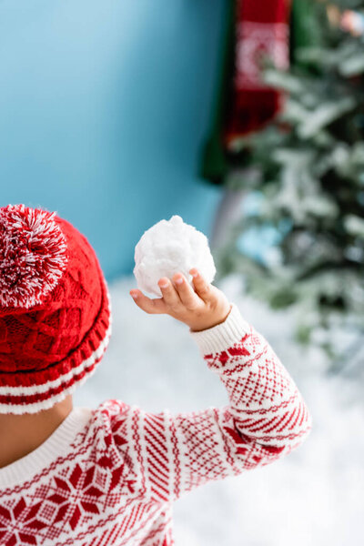 back view of boy in hat holding snowball on blue 