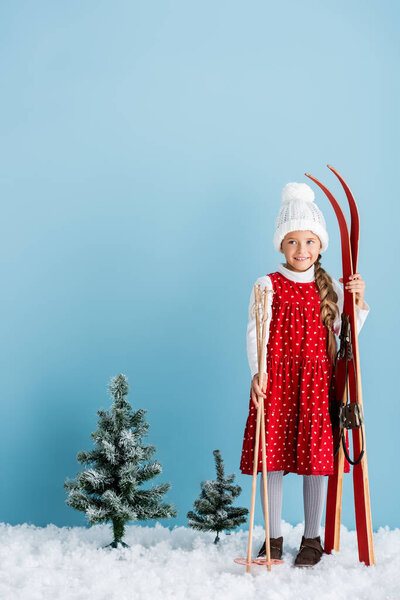 kid in winter outfit standing with ski poles and skis on blue