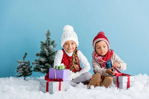 Kinderen Winterkleding Zittend Sneeuw Nabij Cadeautjes Sparren Geïsoleerd Blauw — Stockfoto
