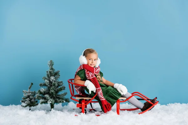 Menina Inverno Earmuffs Cachecol Sentado Trenó Neve Perto Pinheiros Azul — Fotografia de Stock