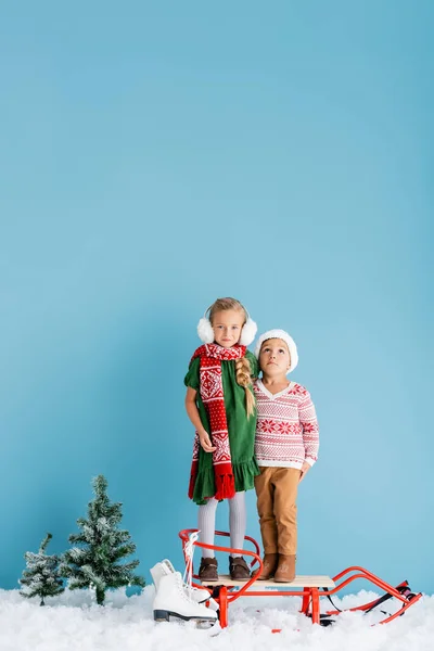 Menina Inverno Earmuffs Trenó Perto Irmão Chapéu Patins Gelo Azul — Fotografia de Stock