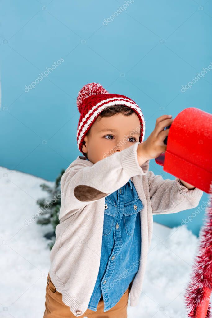 boy in winter outfit reaching red mailbox on blue 