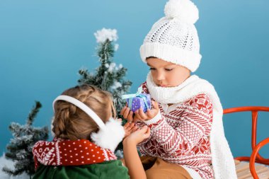 Örgü şapkalı oğlanın seçilmiş odak noktası. Kışın mavi kulaklıklı bir kızın yanında otururken elinde hediye tutuyor.