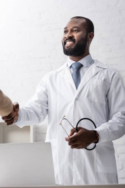 Afrika kökenli Amerikalı doktor steteskop tutuyor ve hastalarla el sıkışıyor.