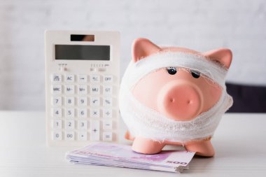Selective focus of piggy bank near euro banknotes and calculator on white table clipart