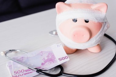 Steteskop yakınındaki domuz kumbarasının seçici odak noktası ve masanın üzerindeki para