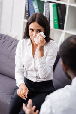 Afro-Amerikan psikoloğun yanında otururken gözlerini kağıt peçeteyle silen ağlayan kadının seçici odağı.