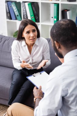 Seçici odak noktası, Afrika kökenli Amerikalı psikoloğun elinde dosya tutarken el kol hareketi yapan gergin kadın.