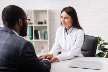 Esmer doktorun seçici odağı. Klinikteki Afrikalı Amerikalı adamın ellerine dokunuyor.