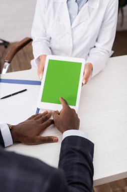 Afro-Amerikan bir adamın yeşil ekranlı dijital tableti işaret ederek doktorun yakınındaki