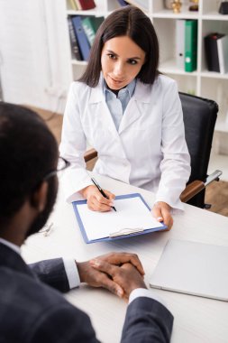 Esmer doktorun seçici odak noktası afro amerikan erkeğinin yanındaki panoya yazı yazması.