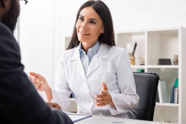 Afrika kökenli Amerikalı bir adamla konuşurken esmer bir doktorun el kol hareketi yapması.