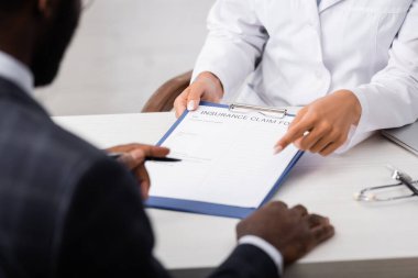 Afrika kökenli Amerikalı bir hastanın elinde kalem tutarken sigorta talebinde bulunan doktoru kısmen işaret etmek.