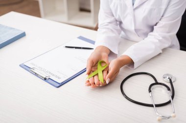 partial view of psychologist holding green awareness ribbon near stethoscope and insurance claim form, mental health concept clipart