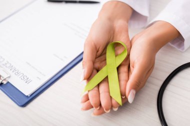 top view of doctor holding green awareness ribbon near insurance claim form, mental health concept clipart