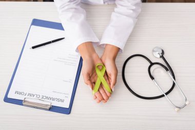top view of psychologist holding green awareness ribbon near insurance claim form and stethoscope, mental health concept clipart