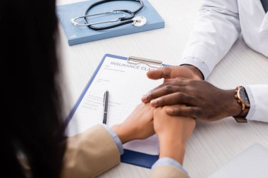 Afro-Amerikan doktorların seçici odak noktası sigorta talep formu ve steteskop ile panonun yanındaki hastanın ellerine dokunmak.