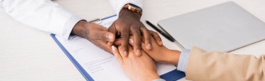Afro-Amerikalı bir doktorun sigorta formuyla panonun yanındaki hastanın ellerine dokunması, panoramik çekim.