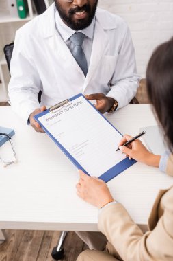 Afrika asıllı Amerikalı bir doktorun yanında sigorta tazminatı imzalayan bir kadın görülüyor.