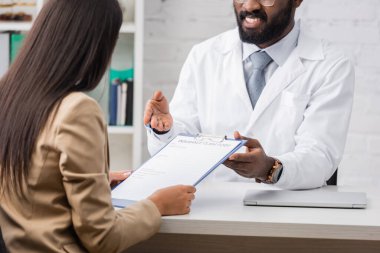 Afrikalı Amerikalı doktorların seçici odak noktası, esmer kadının yanındaki sigorta talep formunu işaret ediyor.