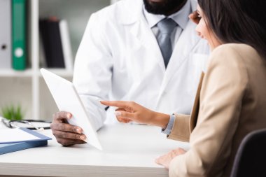 Afro-Amerikalı doktorun elinde dijital tabletle hastayı işaret ederken görüntüsü kesilmiş.