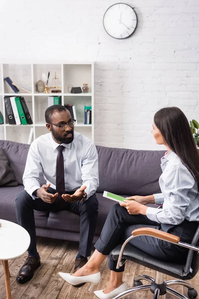 Strese girmiş Afrikalı Amerikalı bir adam, elinde yeşil ekranlı dijital tablet olan bir psikologla konuşuyor.