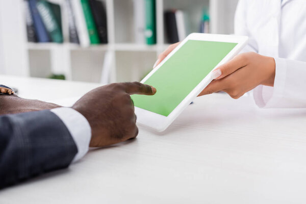 частичный вид африканского американца, указывающего пальцем на цифровой планшет с зеленым экраном рядом с доктором