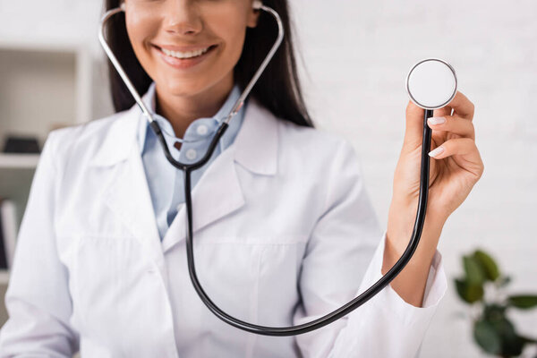 cropped view of joyful doctor holding stethoscope in clinic