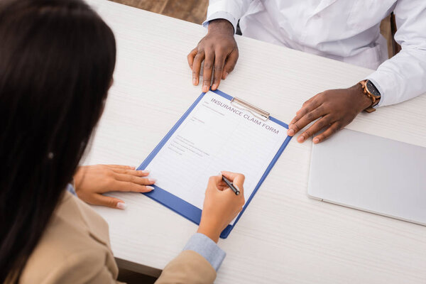 overhead view of patient signing insurance claim form near african american doctor