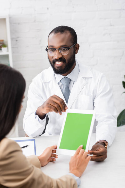 selective focus of woman touching digital tablet with blank screen near african american doctor