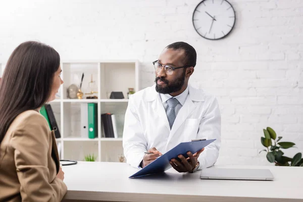 Africano Americano Médico Óculos Segurando Prancheta Perto Mulher Morena — Fotografia de Stock