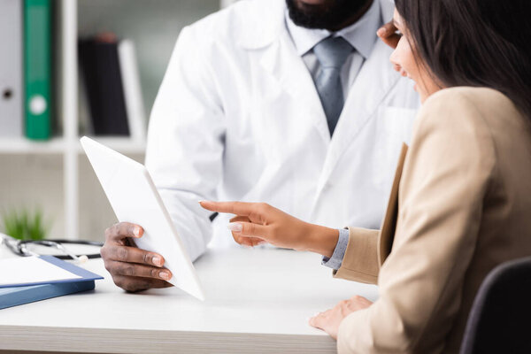 cropped view of african american doctor holding digital tablet near patient pointing with finger