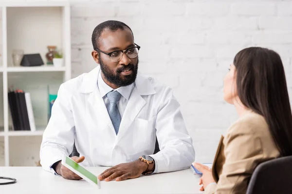 アフリカ系アメリカ人医師の選択的焦点は患者の近くに緑の画面を持つデジタルタブレットを保持眼鏡で — ストック写真