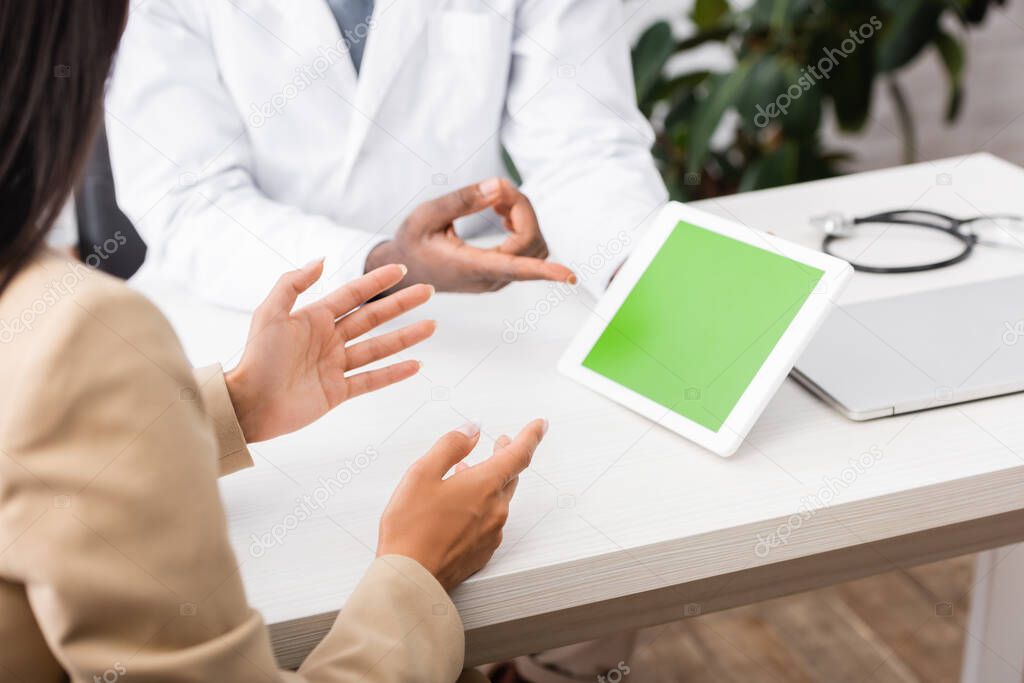cropped view of african american doctor in eyeglasses pointing with finger at digital tablet with green screen