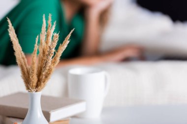 Selective focus of spikelets, books and cup near woman in bedroom  clipart