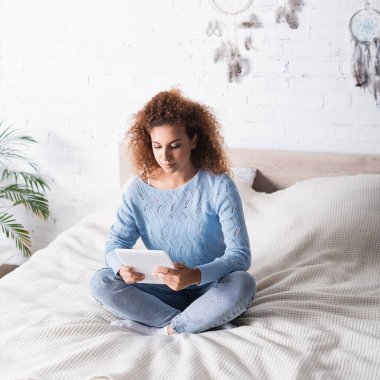 Yatakta dijital tablet kullanan kazaklı kızıl saçlı kadın. 