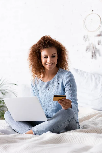 ベッドの上でラップトップを使用している間クレジットカードを見ている女性の選択的な焦点 — ストック写真