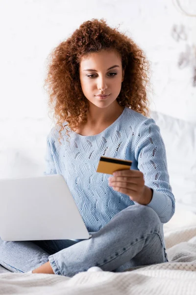 Selective Focus Curly Woman Looking Credit Card While Holding Laptop — Stock Photo, Image