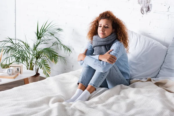 Young woman in scarf feeling cold on bed at home