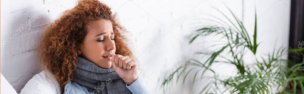 Panoramic shot of woman in scarf coughing at home 