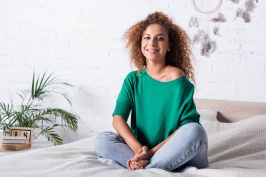 Genç kızıl saçlı kadın evde yatağında kameraya bakıyor. 