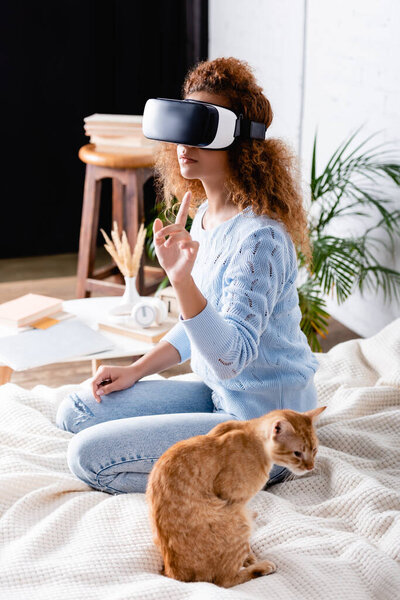 Selective focus of woman using virtual reality headset near cat on bed 