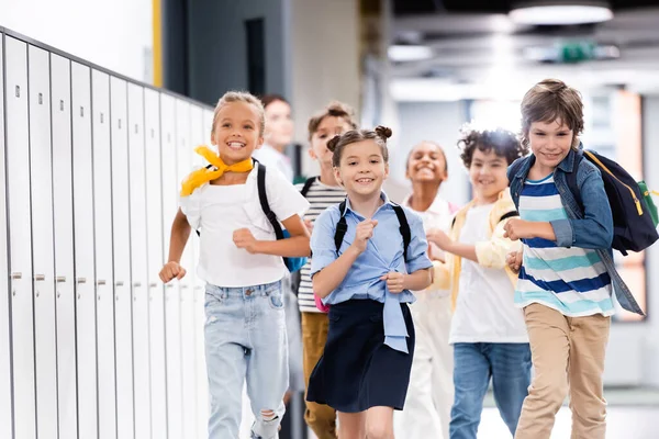 学校の廊下をバックパックが走っている多文化のクラスメートの選択的な焦点 — ストック写真