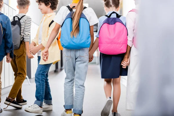 学校の廊下を歩きながら手を取り合っている多民族の同級生の後ろ姿 — ストック写真