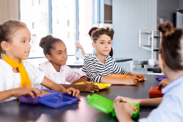 給食ボックスの近くの学校の食堂に座っている多文化の生徒の選択的焦点 — ストック写真