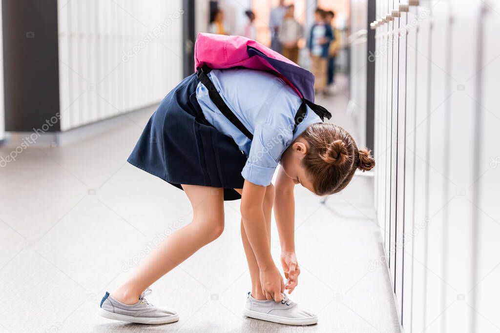 schoolgirl with backpack tying laces on gumshoe in school corridor