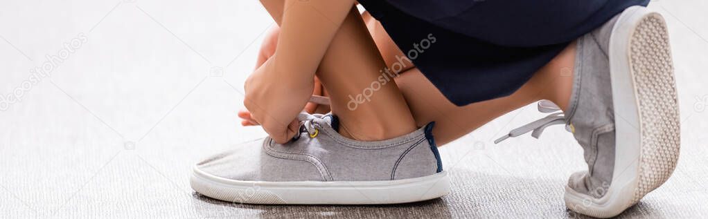 partial view of schoolgirl tying laces on sneaker, panoramic shot