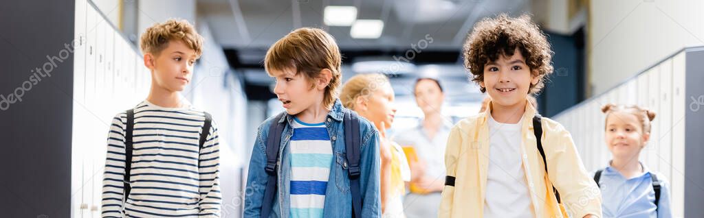 horizontal image of multicultural classmates walking along school corridor with teacher on background