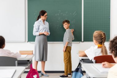 Matematik dersi sırasında tahtada denklemleri çözerken aynı zamanda çok kültürlü sınıf arkadaşlarına bakan okul çocuğu.