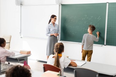 Öğretmen ve çok ırklı öğrencilerin olduğu tahtada denklemleri çözen öğrencilerin arka planı